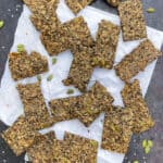 a sheet pan with a square of white parchment, 1 dozen or so rectangular seeded crackers strewn on top