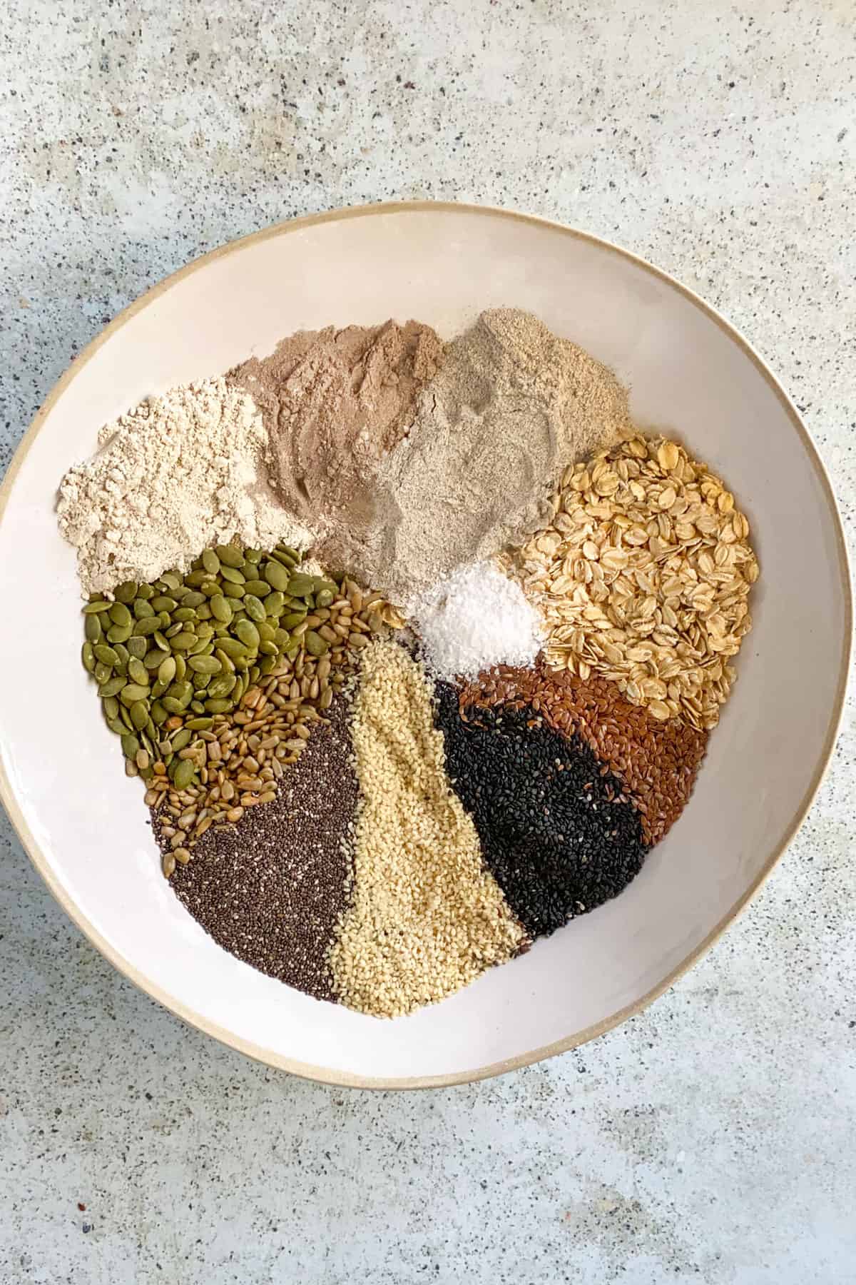 White mixing bowl filled with stripes of colorful seeds and flours poured in.