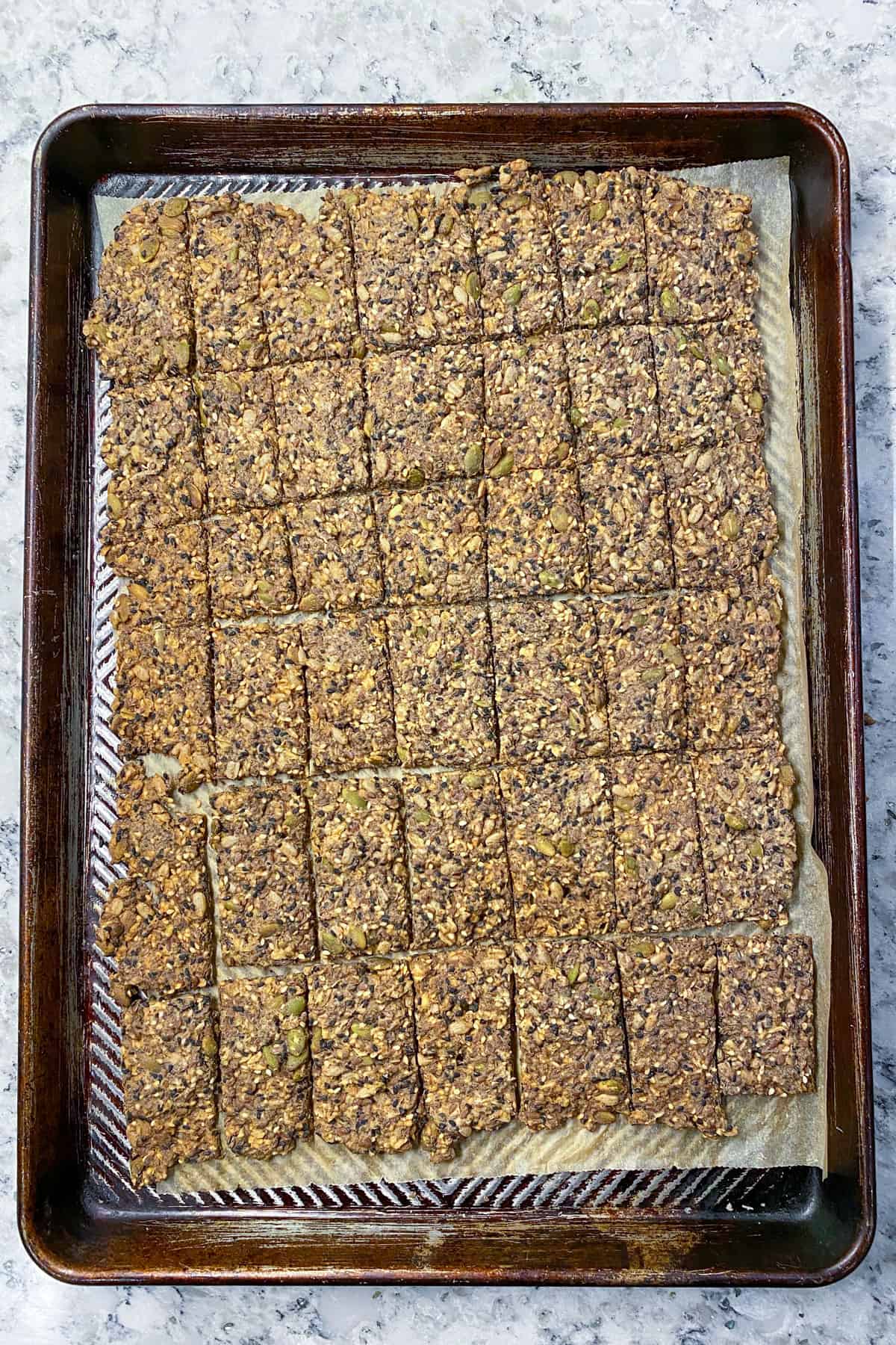 A parchment-lined, rimmed baking sheet seen from above, covered with baked seeded crackers that have been cut into 42 crackers, but haven't yet been separated 