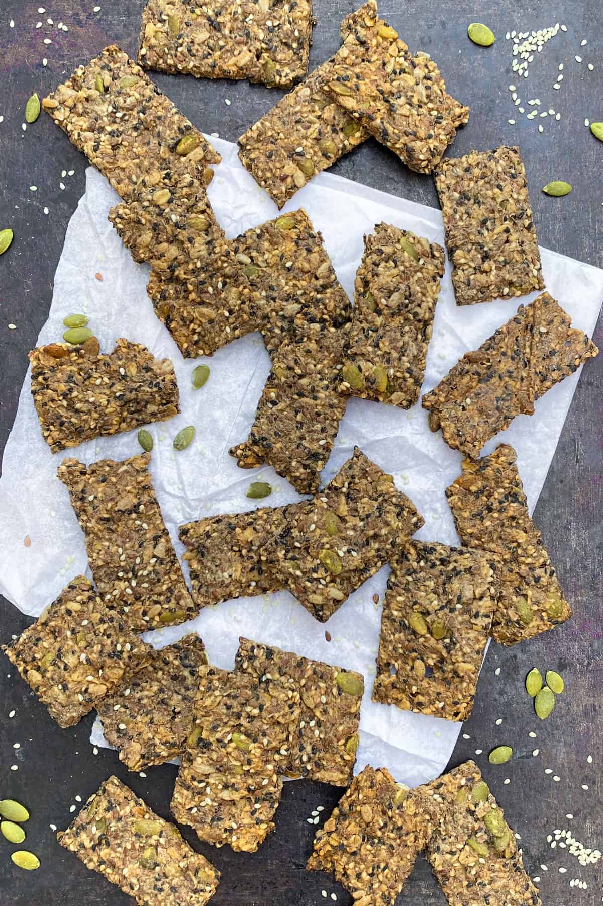 a sheet pan with a square of white parchment, 1 dozen or so rectangular seeded crackers strewn on top