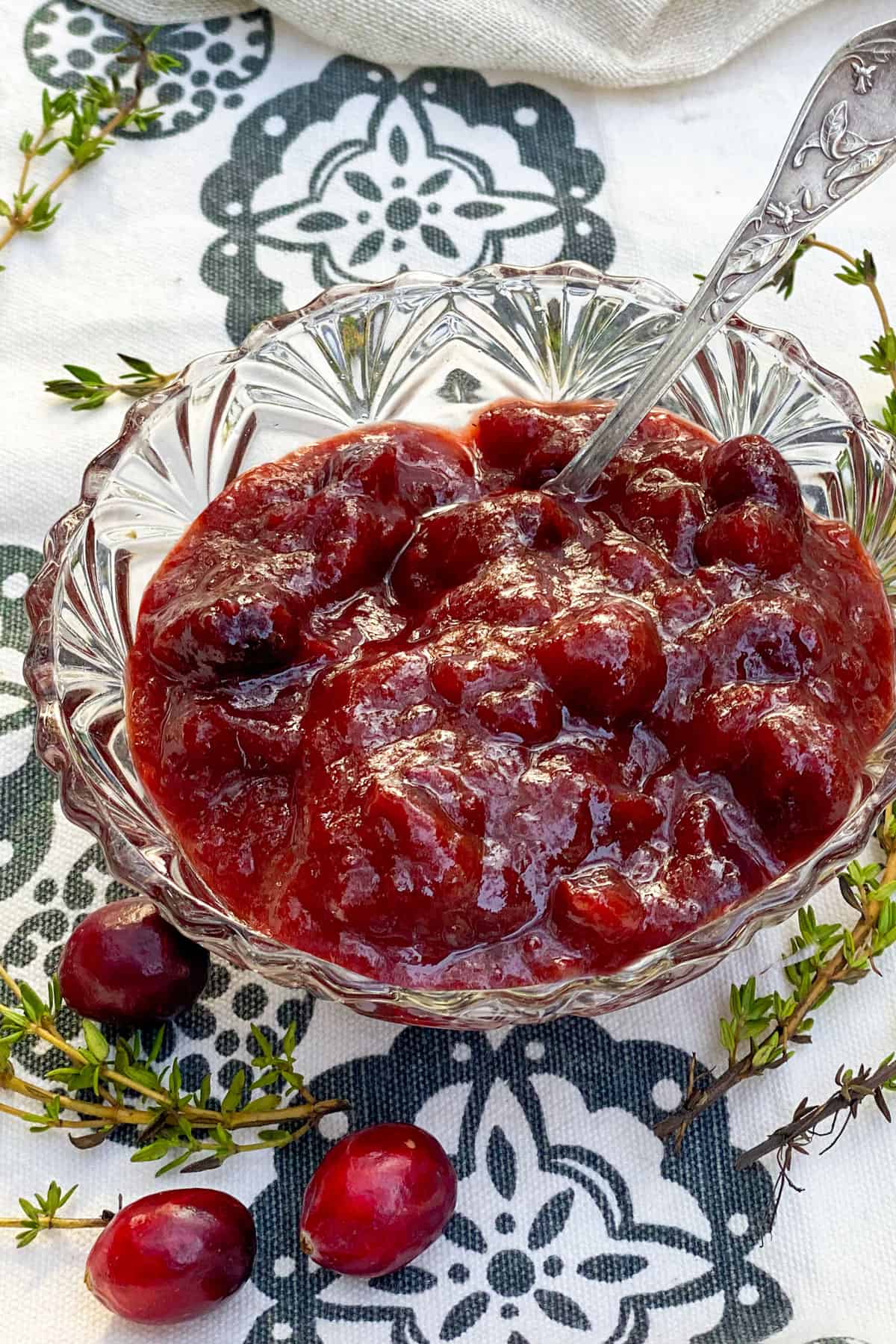 small glass bowl on a black and white cloth napkin, filled with cranberry bourbon bbq sauce, a few cranberries scattered around