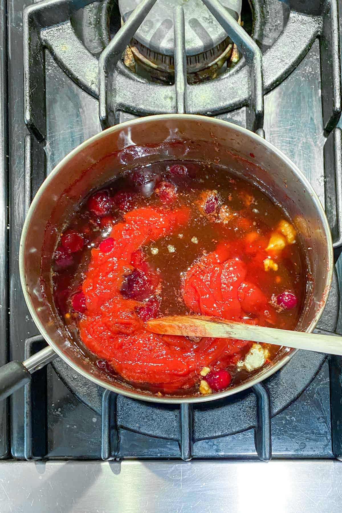 a pot simmering on the stove, filled with raw cranberries plus lots of ingredients for cranberry bourbon bbq sauce, mostly you can see the red ketchup