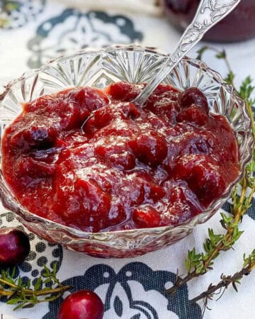 small glass bowl on a black and white cloth napkin, filled with cranberry bourbon bbq sauce, a few cranberries scattered around