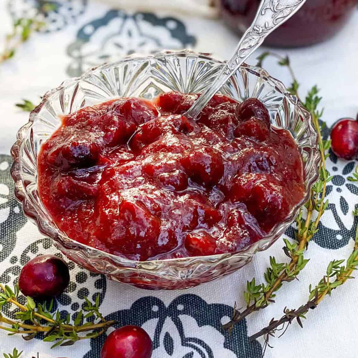 small glass bowl on a black and white cloth napkin, filled with cranberry bourbon bbq sauce, a few cranberries scattered around