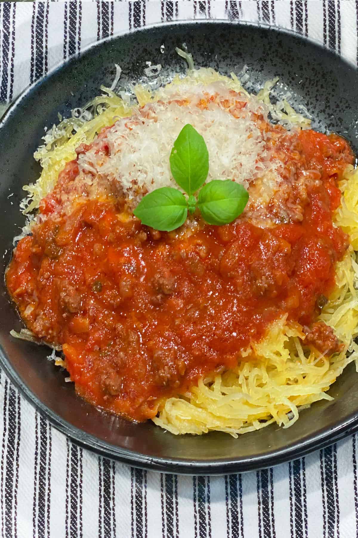 black bowl filled with spaghetti squash topped with meat sauce and a sprig of basil in the middle