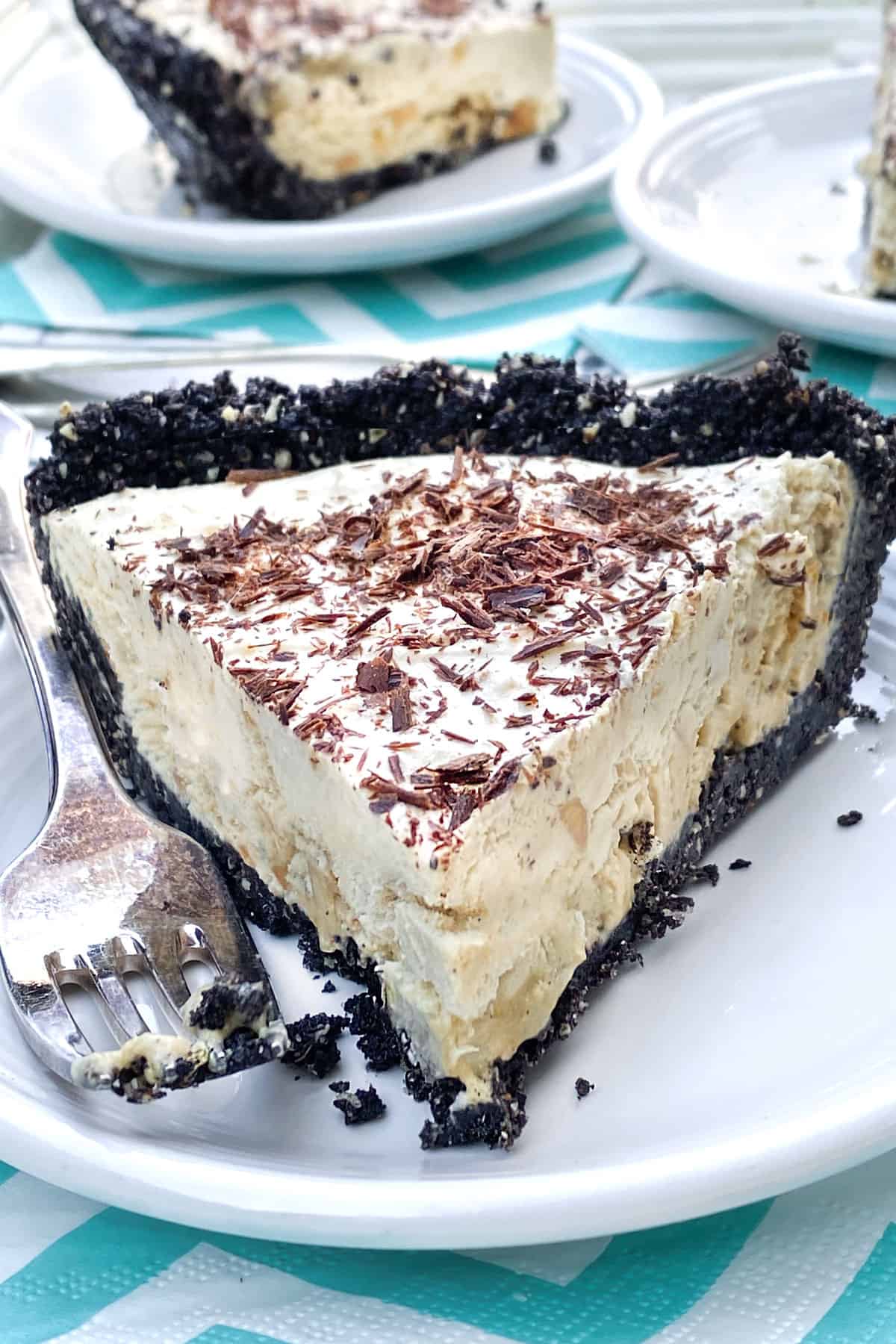 A slice of frozen mocha cream pie with Oreo crust, on a white plate, with a fork on the side