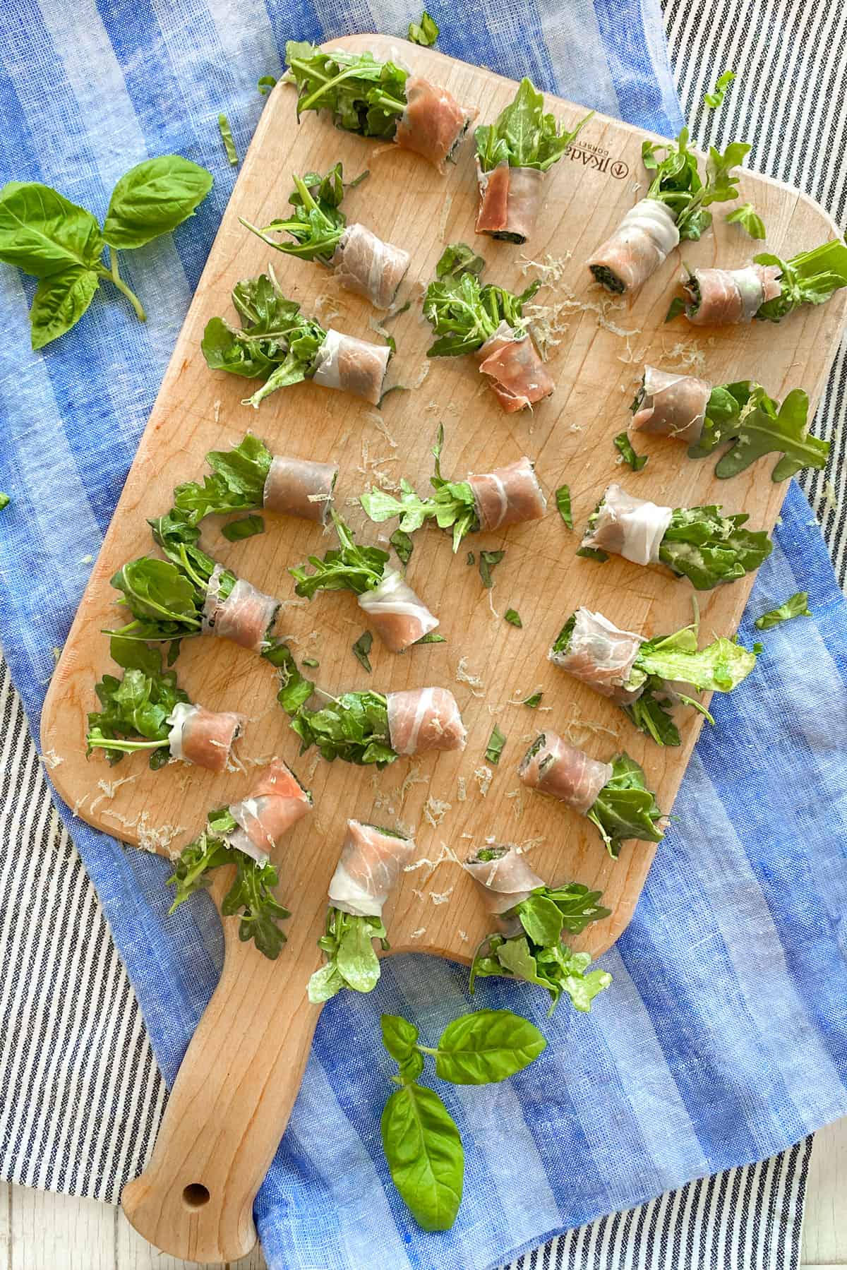 Prosciutto wrapped arugula bundles on a wooden cutting board, seen from above