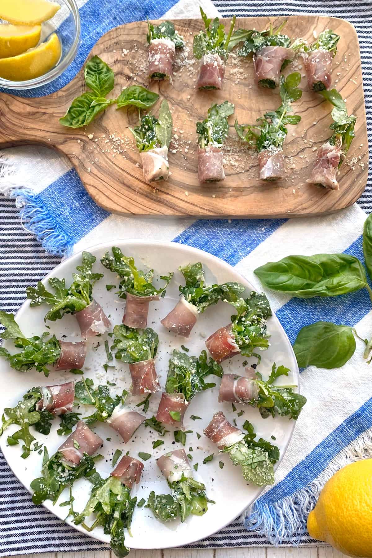 overhead shot of 8 prosciutto wrapped arugula bundles on a wooden cutting board and a round platter with about 16 of the prosciutto bundle