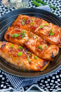 three broiled glazed salmon fillets in a black serving bowl, topped with chopped scallions