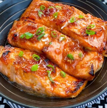 three broiled glazed salmon fillets in a black serving bowl, topped with chopped scallions