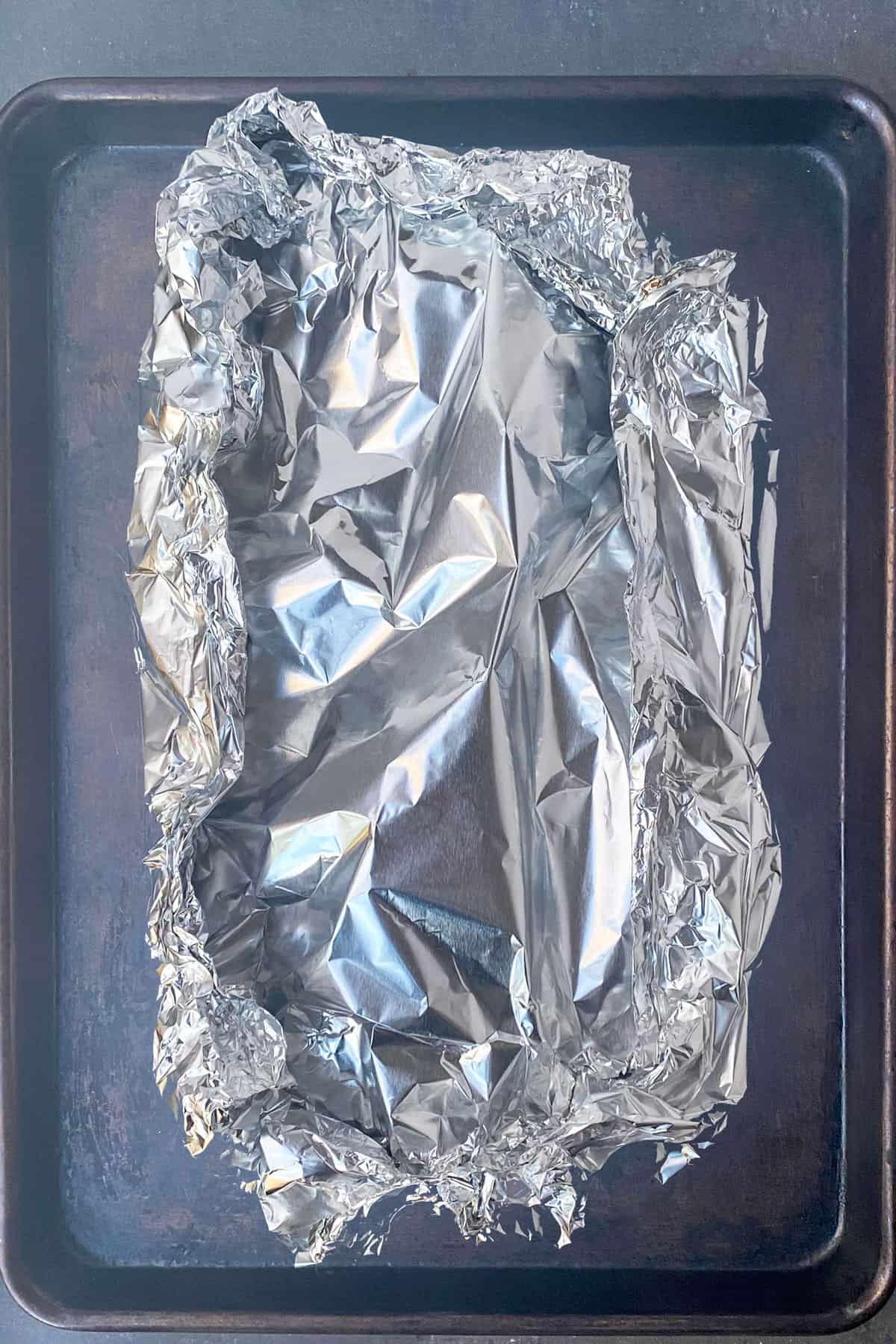 A tinfoil packed sitting on top of a dark baking sheet