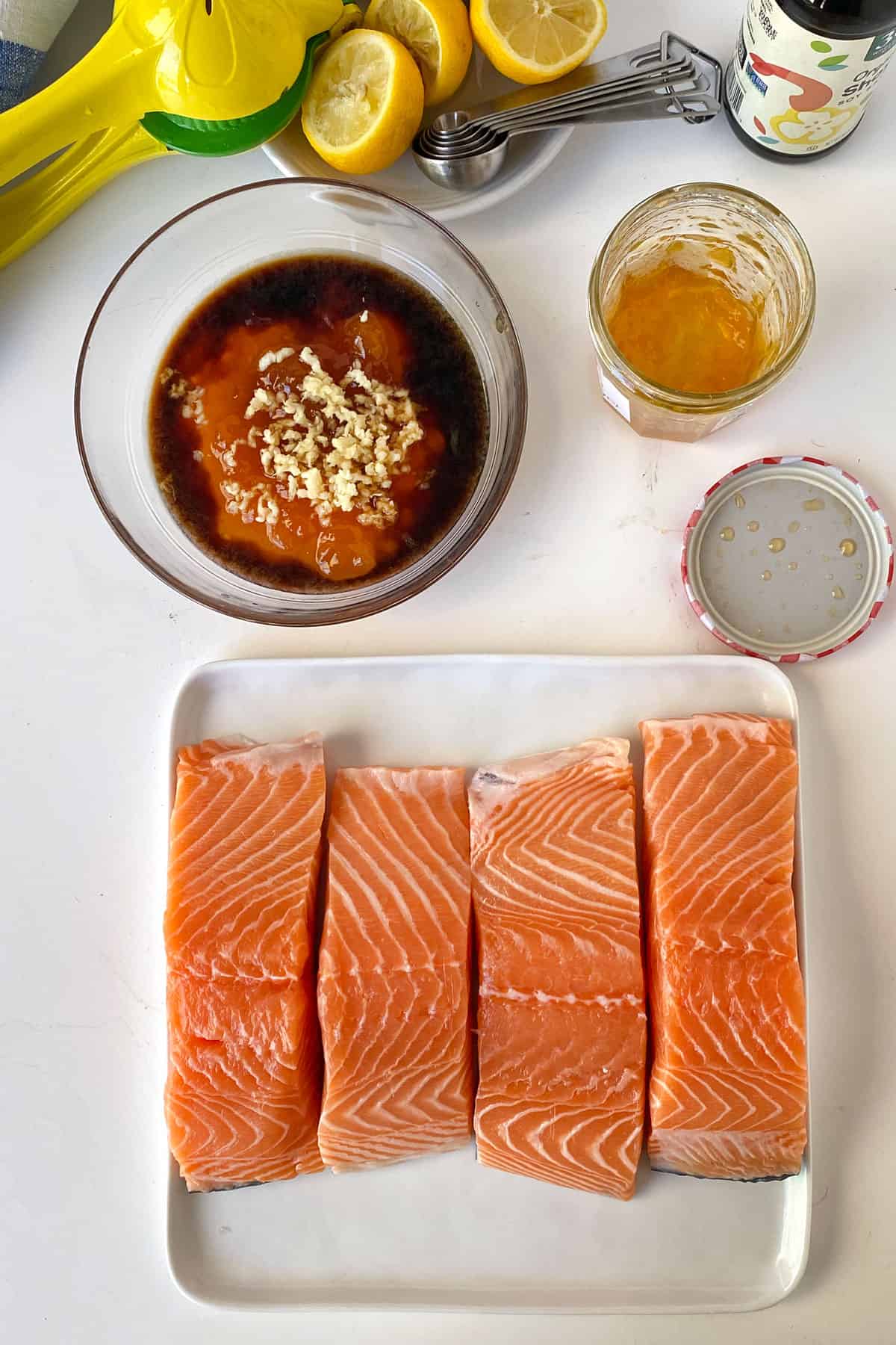 overhead shot of 4 salmon fillets on a plate, a glass bowl filled with soy sauce, apricot preserves, lemon juice and chopped garlic