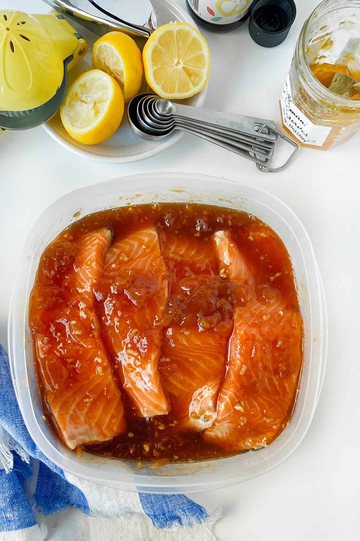 overhead shot of 4 salmon fillets in a square plastic container, coated in apricot marinade/glaze