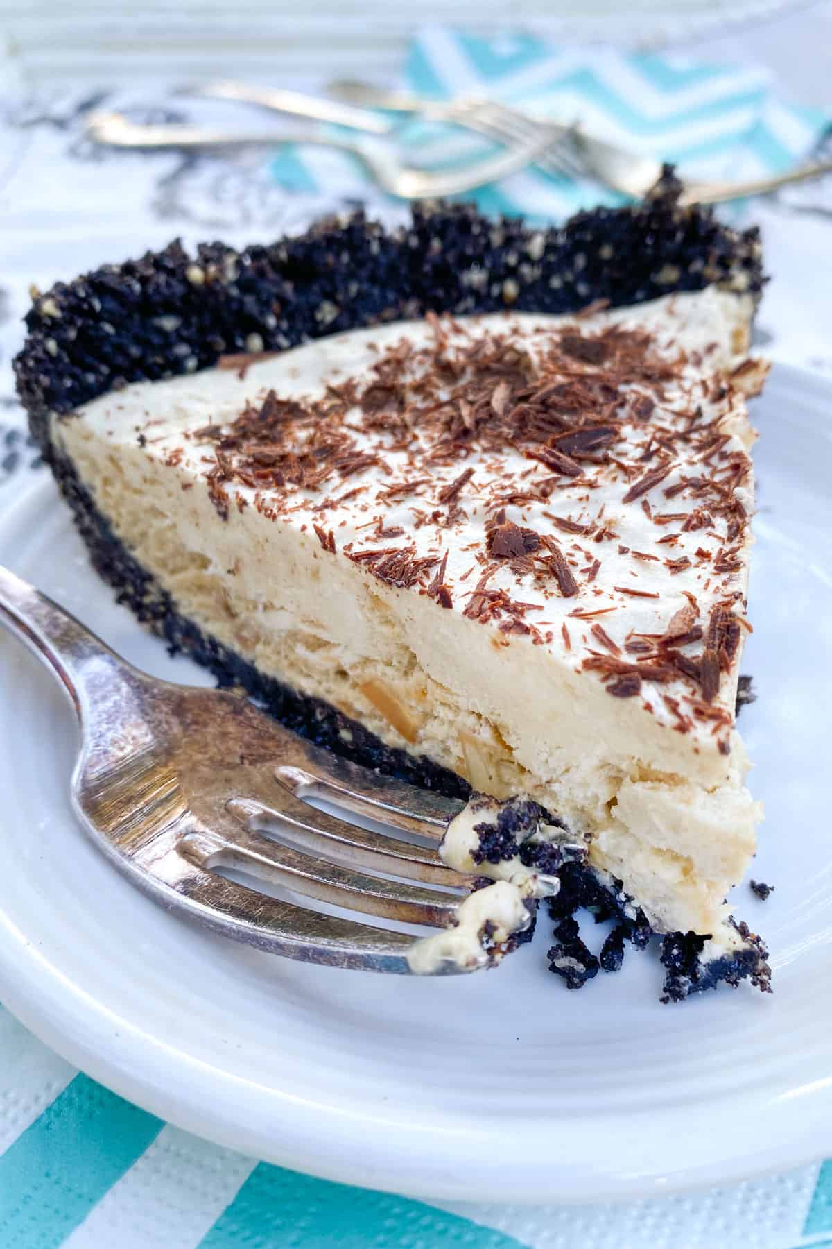 A slice of frozen mocha cream pie with Oreo crust, on a white plate, with a fork on the side