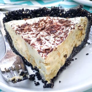 A slice of frozen mocha cream pie with Oreo crust, on a white plate, with a fork on the side