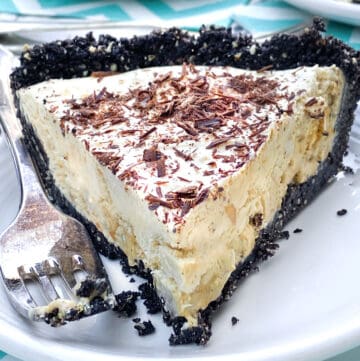 A slice of frozen mocha cream pie with Oreo crust, on a white plate, with a fork on the side