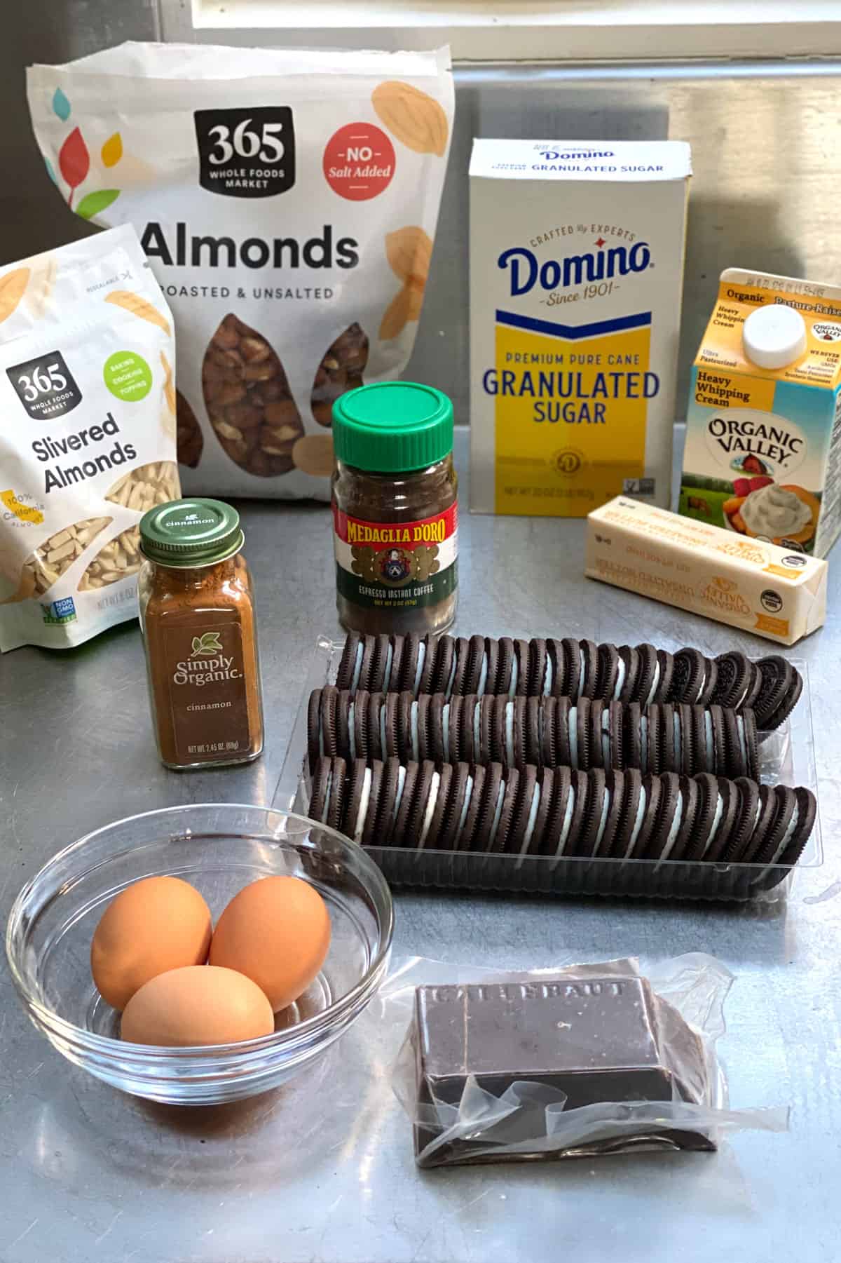 ingredients for frozen mocha cream pie with cookie crumb crust: a container of heavy cream, a pack of Oreos, a box of white sugar, a jar of cinnamon, a bag of whole almond, bag of slivered almonds bar of butter and container of instant coffee, and a block of chocolate