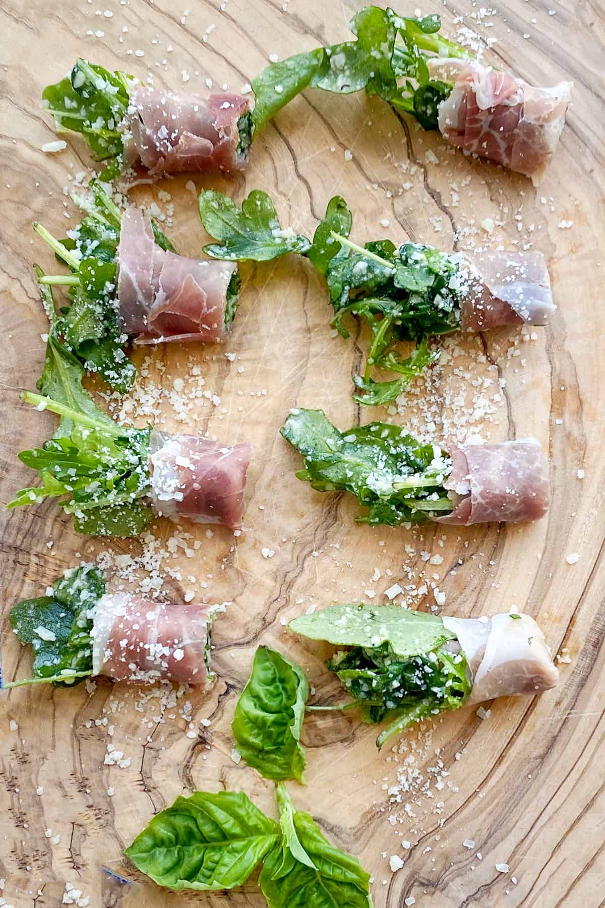 overhead shot of 8 prosciutto wrapped arugula bundles on a wooden cutting board