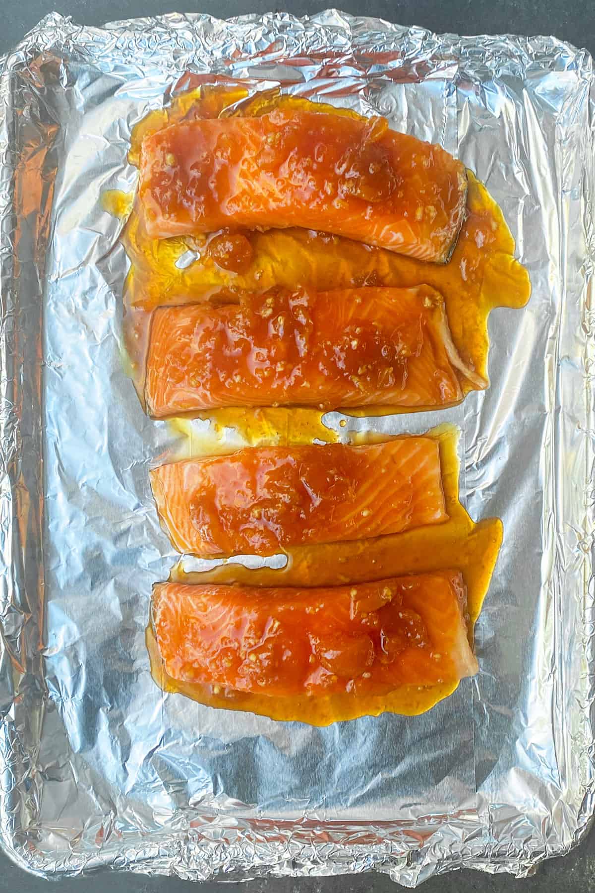 4 salmon fillets topped with apricot glaze, on a tin foil lined baking sheet, seen from above.