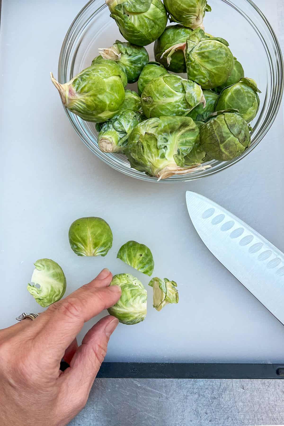 showing how to trim brussels sprouts. Overhead shot of a knife and a hand holding brussel sprout that has had the end trimmed off