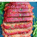 overhead shot of a tomato glazed meatloaf, sliced and set on a black platter and sprinkled with chopped parsley