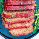 overhead shot of a tomato glazed meatloaf, sliced and set on a black platter and sprinkled with chopped parsley