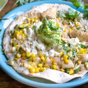 crisp tortilla topped with corn, piece of chicken, avocado crema and cilantro