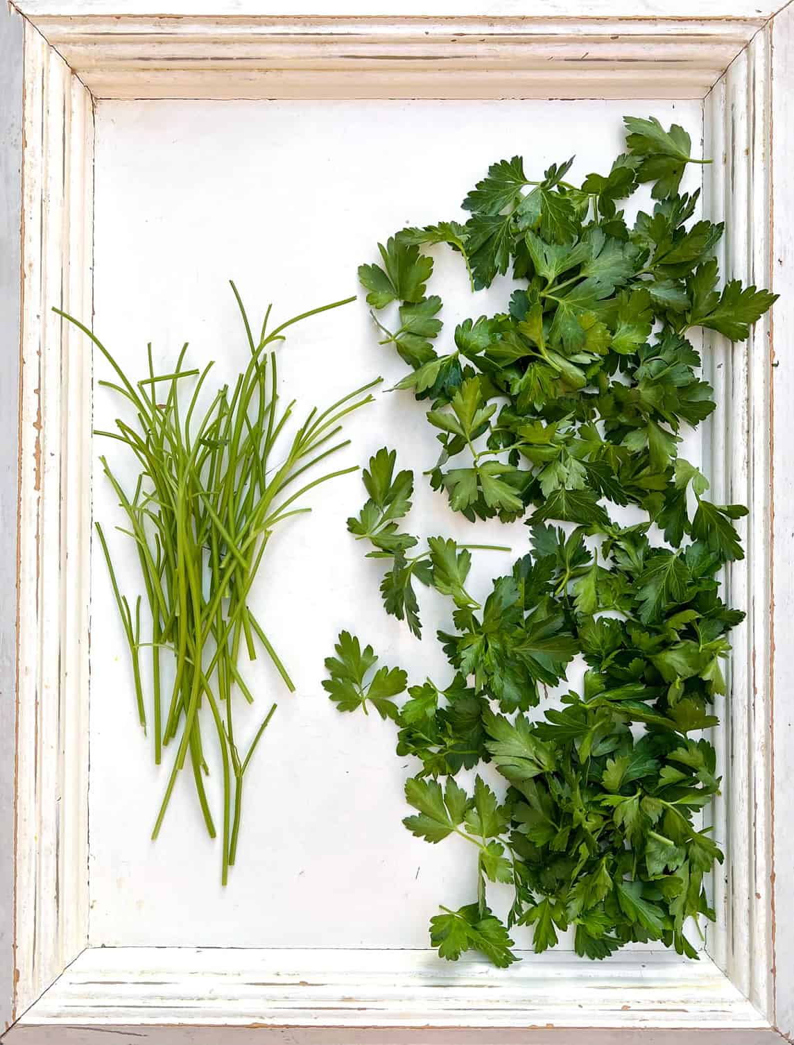 overhead shot of a white wooden tray with parsley stems on the left side and parsley leaves on the right