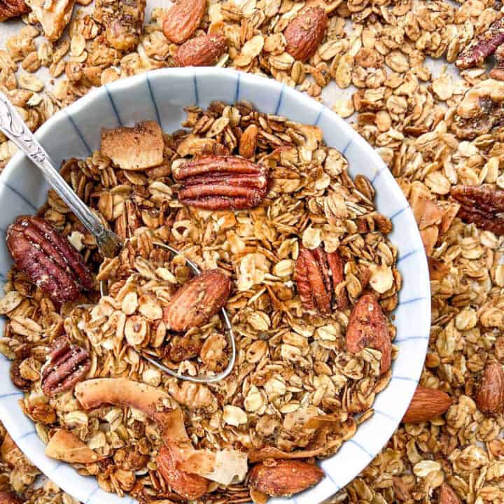 bowl of toasted golden brown granola with pecans, almonds and walnuts, sitting on a sheet pan with more granola.