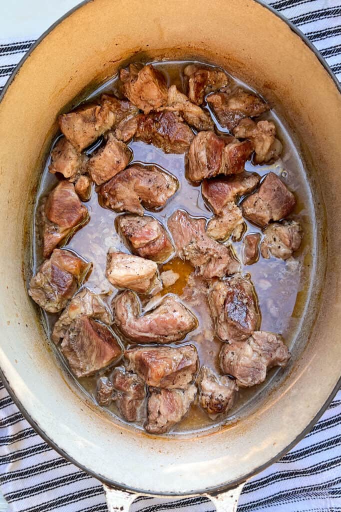 overhead shot of a white oval Dutch oven filled with braised chunks of pork shoulder surrounded with braising juices