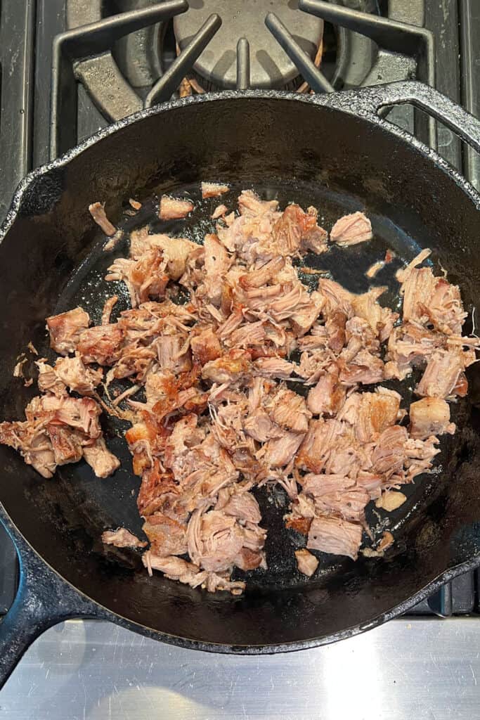 overhead shot of black cast iron skillet filled with pork carnitas that is being crisped up.