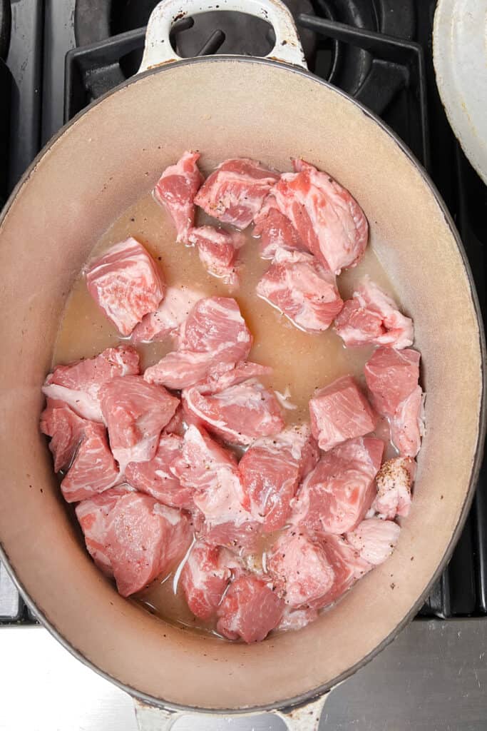 overhead shot of a white dutch oven filled with chunks of pork shoulder sitting in chicken broth