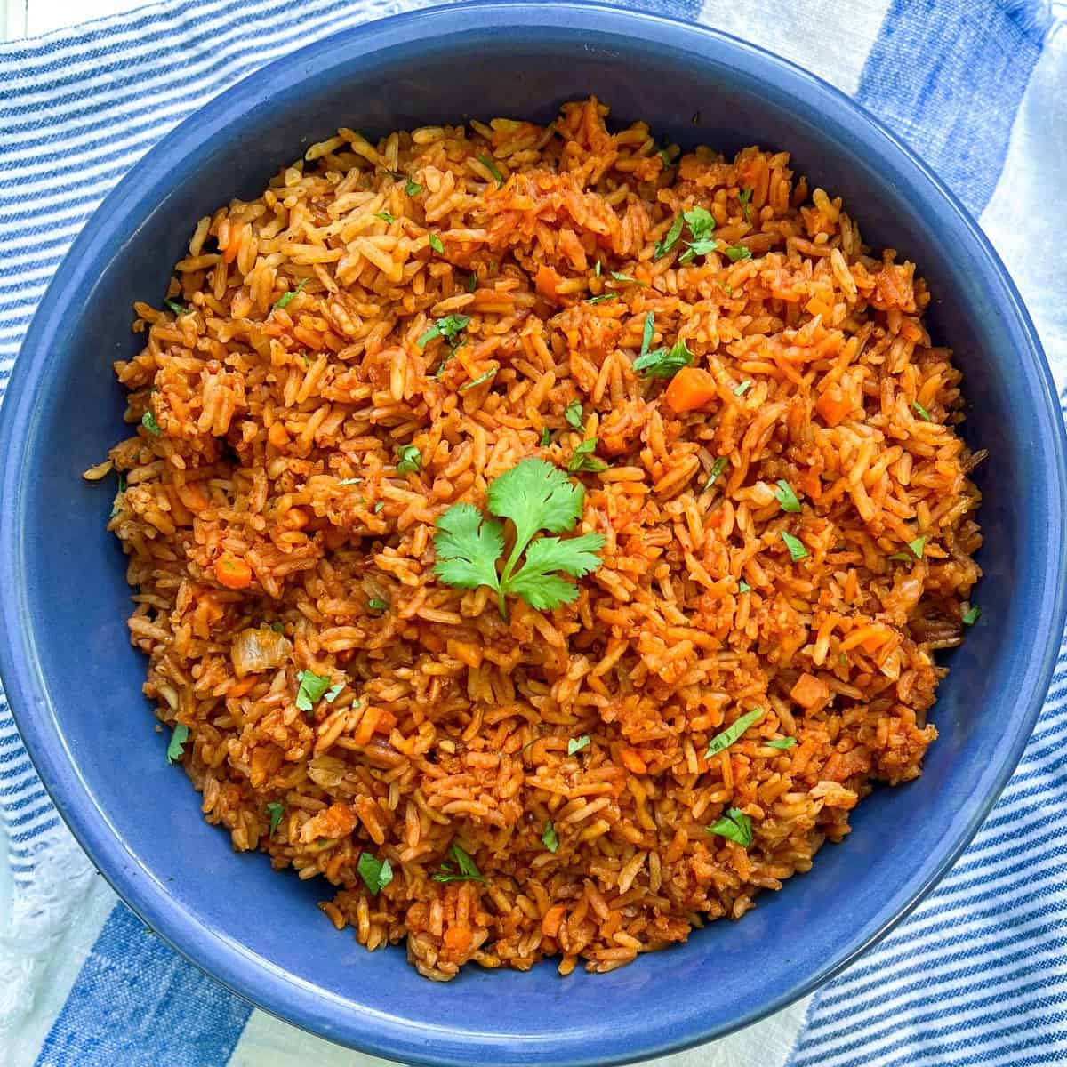 overhead close up of a vivid blue bowl filled with Mexican red rice, sprinkled with chopped cilantro and a cilantro leaf in the center