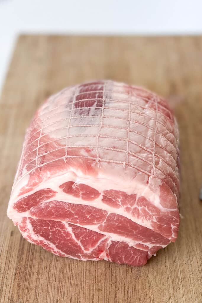 A whole raw boneless pork shoulder roast sitting on a wooden cutting board