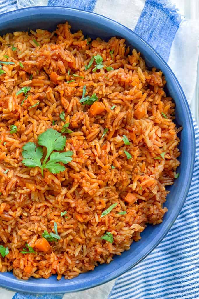 overhead close up of a vivid blue bowl filled with Mexican red rice (arroz rojo), sprinkled with chopped cilantro and a cilantro leaf in the center