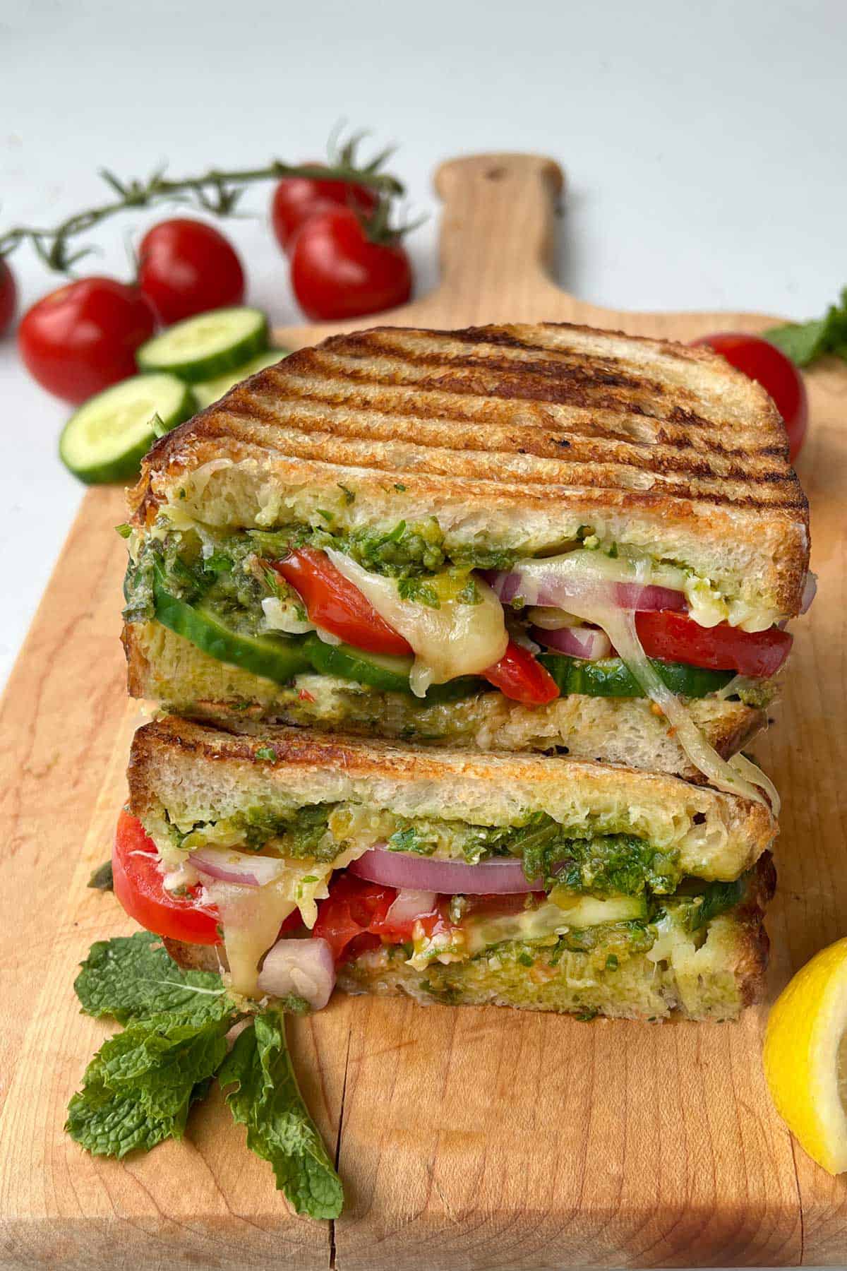 two halves of a cheesy veggie sandwich stacked on top of each other on a wooden cutting board