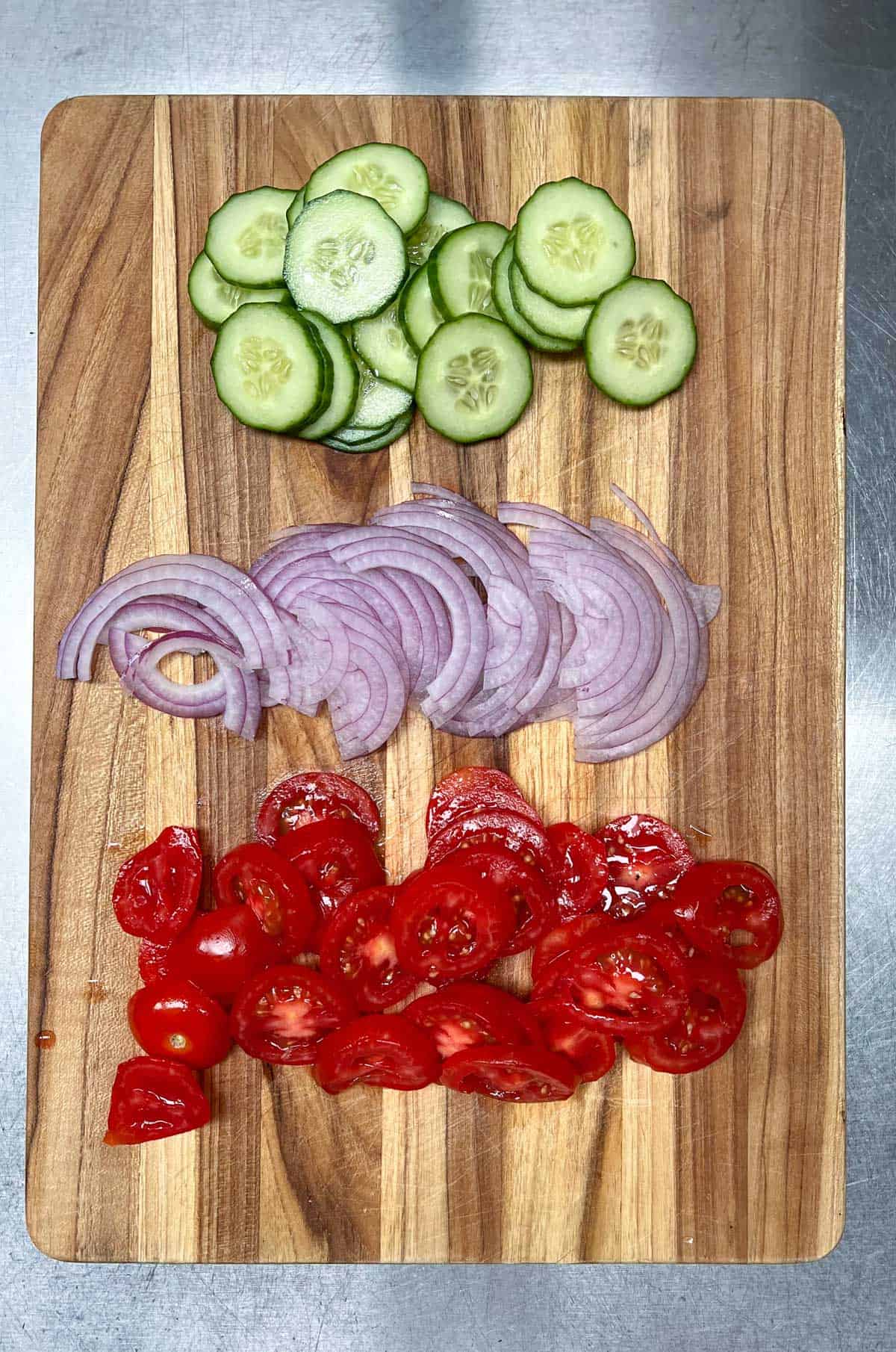 sliced cucumbers, red onions and tomatoes on a cutting board