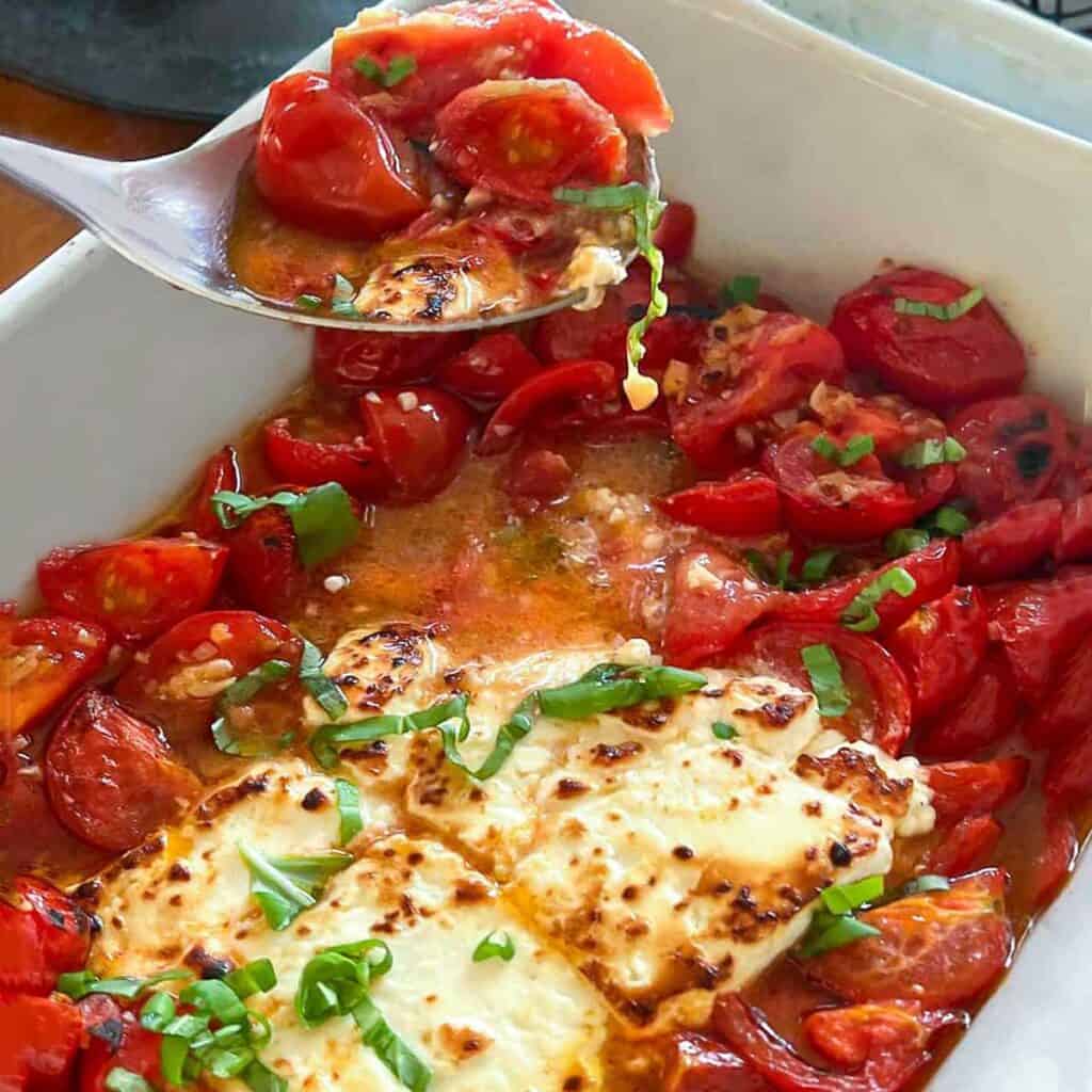 hunks of broiled feta in a white casserole dish surrounded by sautéed cherry tomatoes