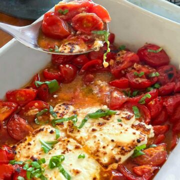 hunks of broiled feta in a white casserole dish surrounded by sautéed cherry tomatoes