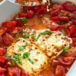 hunks of broiled feta in a white casserole dish surrounded by sautéed cherry tomatoes