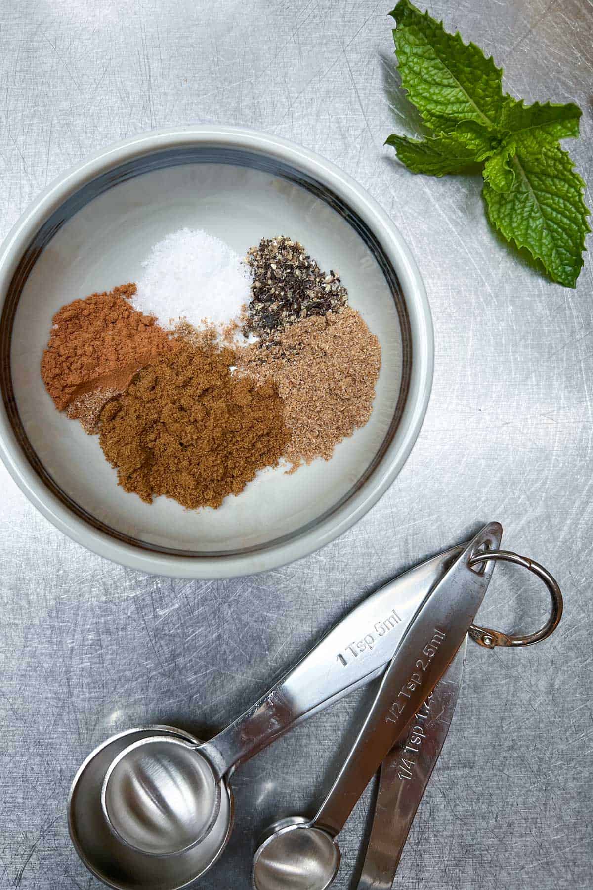 5 different spices in a bowl next to measuring spoons