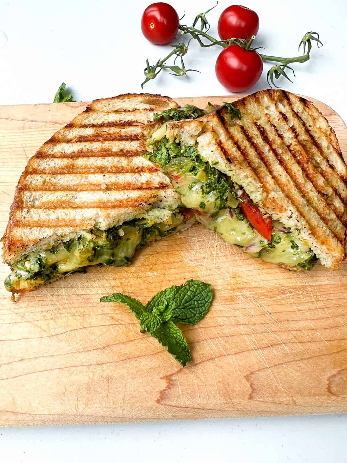 cheese panini grilled Mumbai sandwich on wooden cutting board with 3 cherry tomatoes in the backgrouind