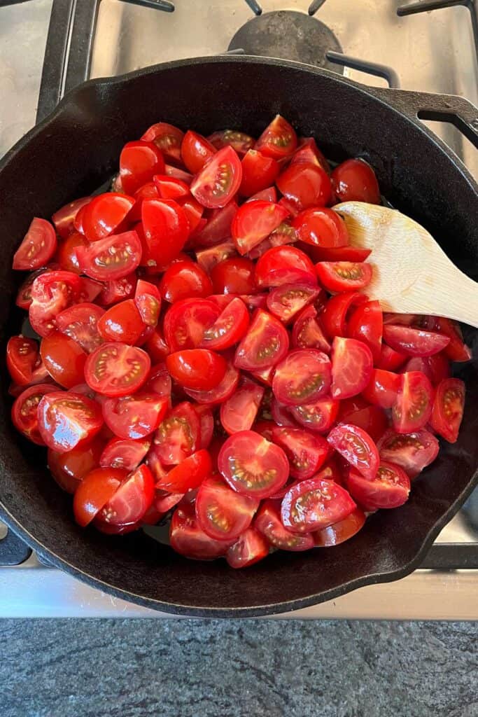 quartered raw cherry tomatoes in a cast iron skillet with a wooden spoon