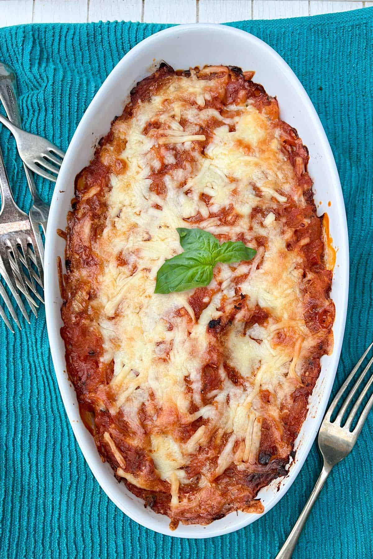 white oval casserole of spaghetti squash and tomato sauce with melted cheese on top and a sprig of basil