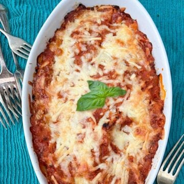 white oval casserole of spaghetti squash and tomato sauce with melted cheese on top and a sprig of basil