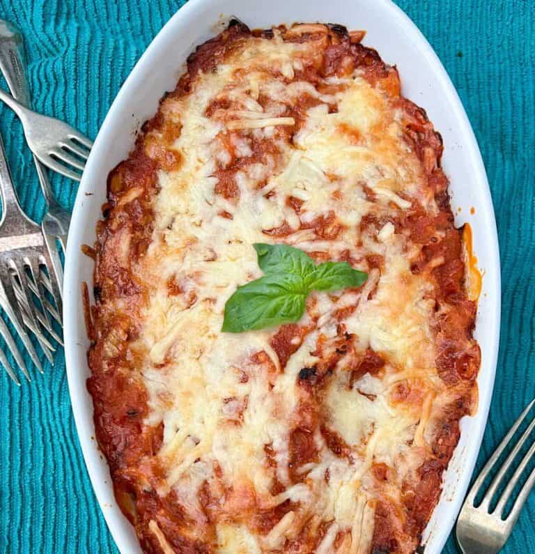 white oval casserole of spaghetti squash and tomato sauce with melted cheese on top and a sprig of basil