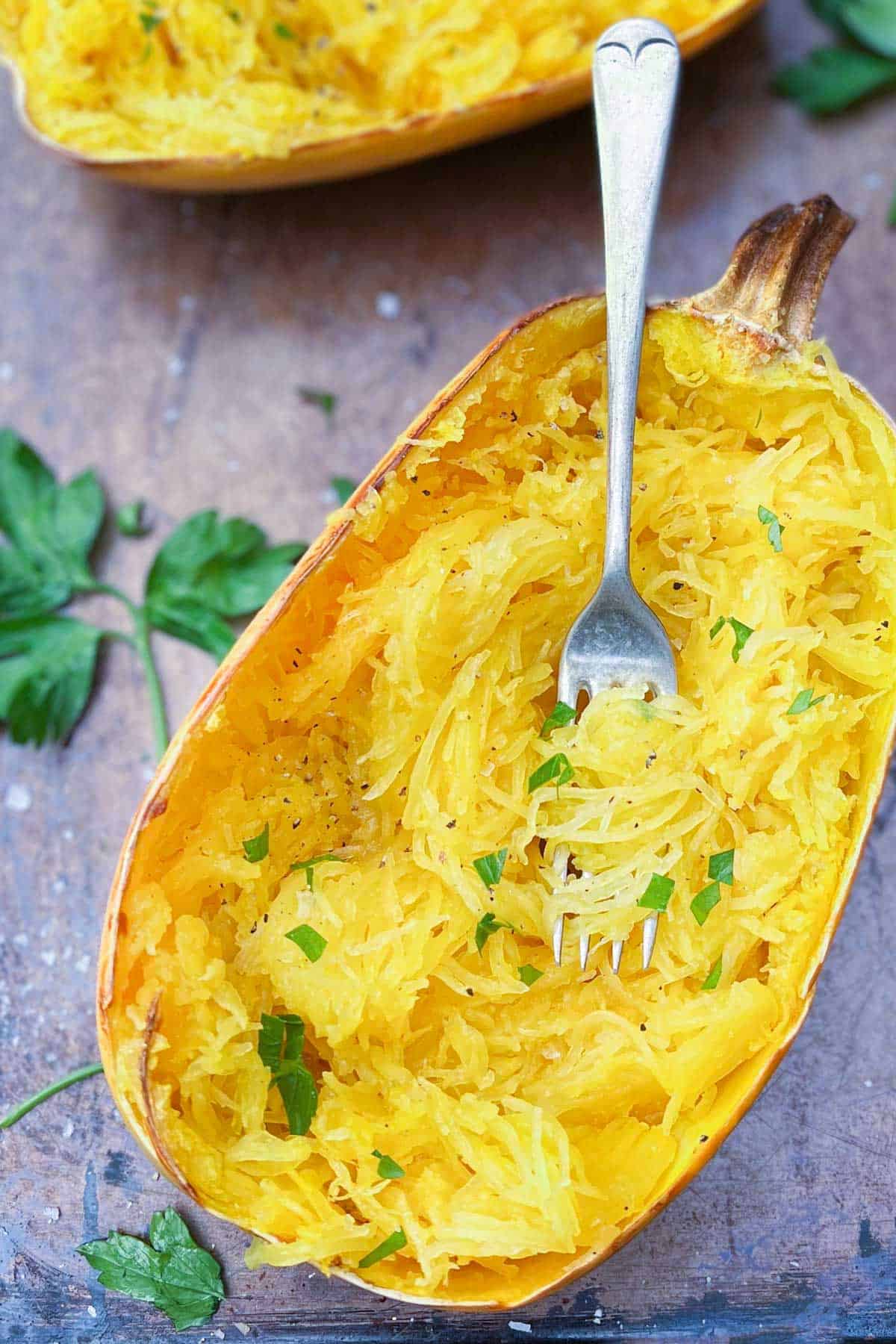 Roasted spaghetti squash  half with a fork twirling the strands and parsley sprinkled on top