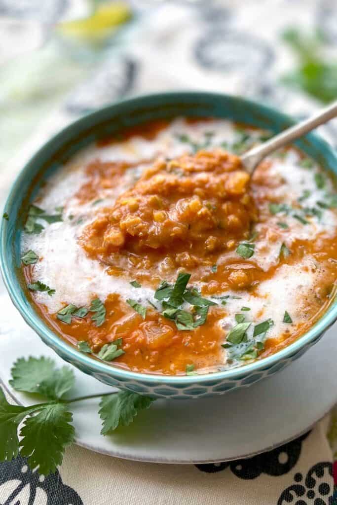 blue bowl filled with red lentil soup drizzled with coconut milk and sprinkled with chopped cilantro