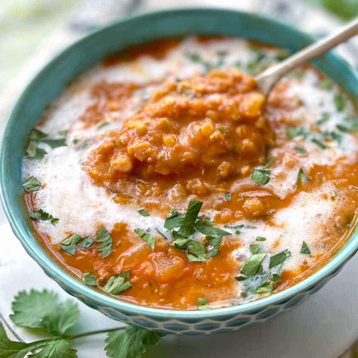 blue bowl filled with red lentil soup drizzled with coconut milk and sprinkled with chopped cilantro