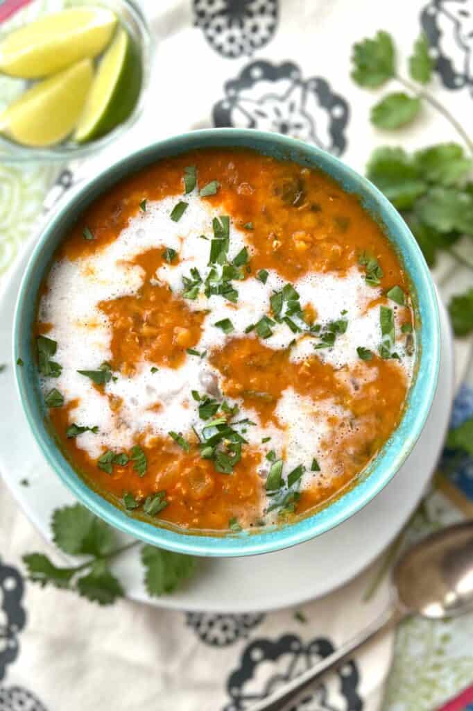 blue bowl filled with red lentil soup drizzled with coconut milk and sprinkled with chopped cilantro